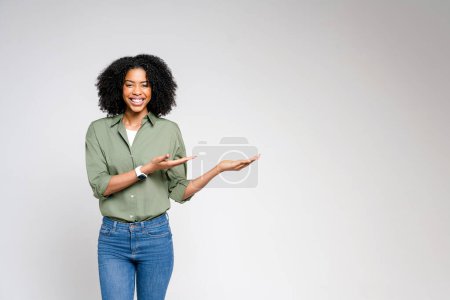 A dynamic African-American woman points with confidence, her joyful expression and casual business attire against a neutral background conveying a message of positive engagement and approachability.
