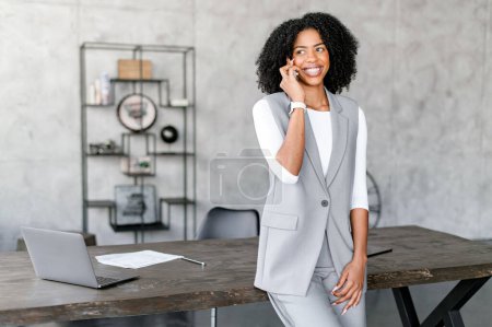 An ebullient African-American businesswoman engages in a phone call, her stance and bright smile reflecting a confident negotiation or positive news