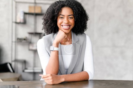 With her chin resting thoughtfully on her hand, this African-American businesswomans friendly demeanor and relaxed posture at her office desk present a blend of professionalism and approachability.