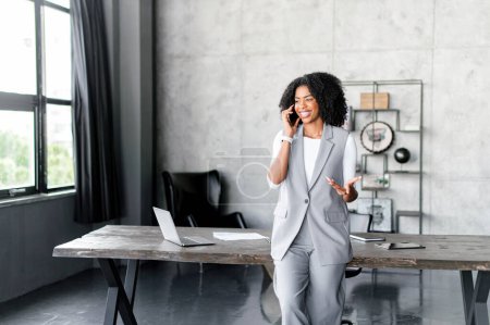 Téléchargez les photos : Une femme d'affaires afro-américaine charismatique parle sur son téléphone dans un bureau moderne, son geste de la main ajoute du dynamisme à la conversation. Un professionnel prospère en pleine discussion - en image libre de droit