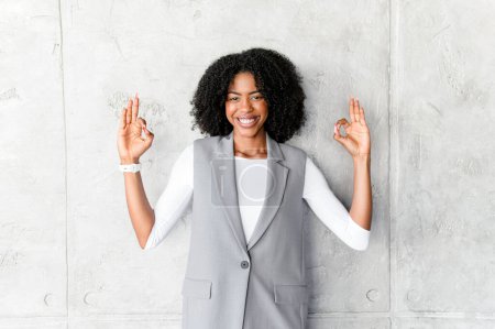 Gesturing OK with both hands, this confident African-American businesswoman communicates assurance and positivity, embodying professional excellence and reliability