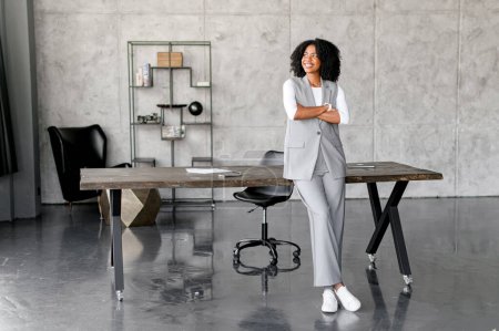 Standing by a sleek office desk, this African-American businesswoman exudes confidence and modernity, with a minimalist office space providing a professional backdrop.