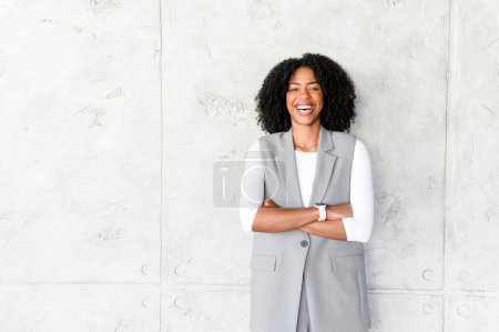 Photo for A beaming African-American woman stands confidently, her arms crossed, in a stylish business-casual vest and white long-sleeve shirt, representing a blend of modern professionalism and approachability - Royalty Free Image