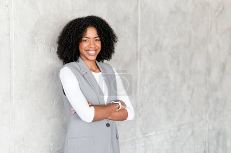 A radiant smile from the businesswoman as she leans casually against a textured backdrop, her grey vest ensemble perfectly balancing professionalism with a relaxed demeanor.