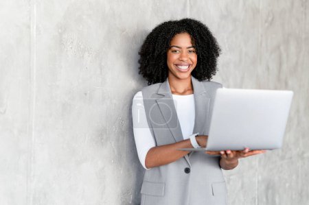 La confiance rayonne du professionnel afro-américain des affaires alors qu'elle tient son ordinateur portable, un mélange parfait de professionnalisme occasionnel et d'intelligence technico-avertie