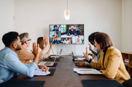 Diverse team of professionals enthusiastically participates in a video conference call, waving hands, reflecting a warm and inclusive company culture that embraces remote collaboration and team unity