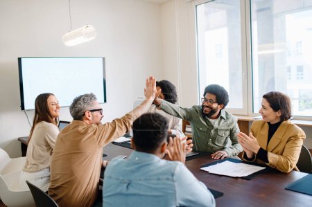 A spirited office team engages in a high-five, highlighting the successful collaboration and energetic atmosphere. Teamwork and the collective success that comes from a well-coordinated effort.