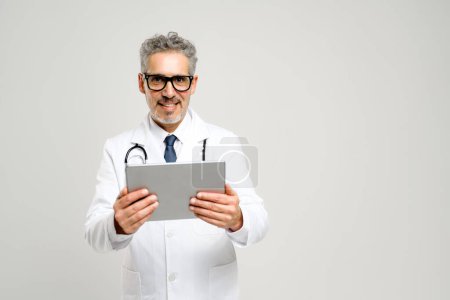 Vertieft in Inhalte auf Tablets, repräsentiert dieser leitende Arzt das moderne Gesicht des Gesundheitswesens, wo digitale Werkzeuge dabei helfen, informierte medizinische Entscheidungen zu treffen. Gesundheitswesen mit modernster Technologie