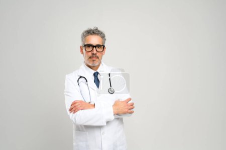 Un médecin mature se tient en confiance sur un fond blanc, bras croisés, symbolisant une approche inébranlable des soins aux patients et du professionnalisme médical.