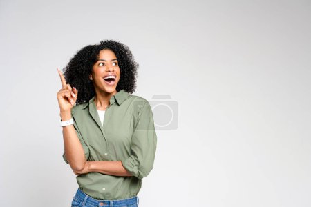 Radiating joy, an African-American woman points upwards, her face alight with excitement, indicating a new idea or a joyful exclamation on a plain backdrop