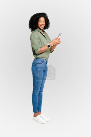 African-American woman with a warm smile, casually typing on her smartphone, reflecting the everyday utility of technology in personal communication