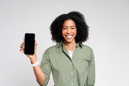 Beaming with joy, this African-American woman showcases her phone with empty screen, advertising concept