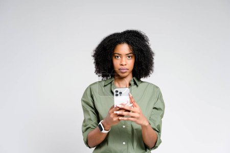 Foto de Una elegante mujer afroamericana está compuesta, sosteniendo un teléfono inteligente en ambas manos con una expresión seria, retratando un comportamiento profesional - Imagen libre de derechos