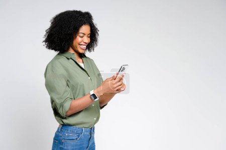 Femme afro-américaine dégage une élégance décontractée en lisant du contenu sur son smartphone, son visage éclairé d'un sourire doux et authentique. , parfait pour un tournage axé sur le style de vie