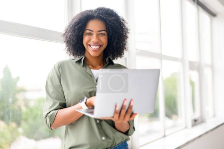 An exuberant young professional woman engages with her laptop, participating in a video conference, her smile reflecting the positive nature of modern communication technology