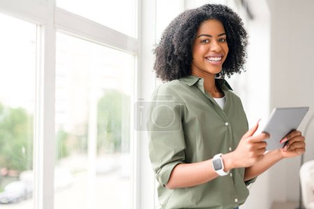 An African-American woman in a relaxed pose, holding a tablet with a confident smile, interacting with friends online or conducting business remotely, highlighting the flexibility of digital devices.