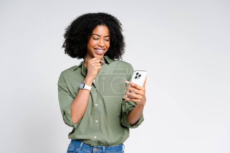 Eine strahlende Afroamerikanerin, die mit ihrem Smartphone hantiert, strahlt Zuversicht und Glück aus und illustriert den modernen, vernetzten Lebensstil auf reinem weißen Hintergrund perfekt..