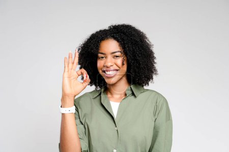Téléchargez les photos : Une femme afro-américaine exubérante montre le geste de la main OK, son visage allumé avec un sourire amical. Cette image incarne parfaitement les thèmes de l'accord et de l'assurance qualité - en image libre de droit