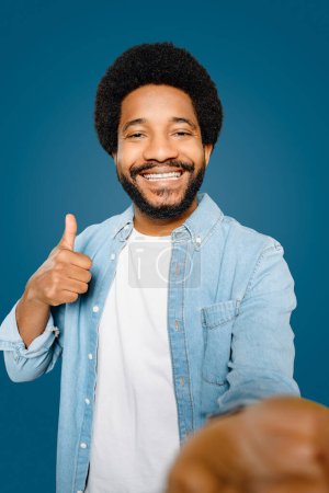 Friendly man gives a thumbs-up to the camera while taking a selfie, his beaming smile suggesting confidence and satisfaction, perfect for promoting positive experiences or services. Like-gesture