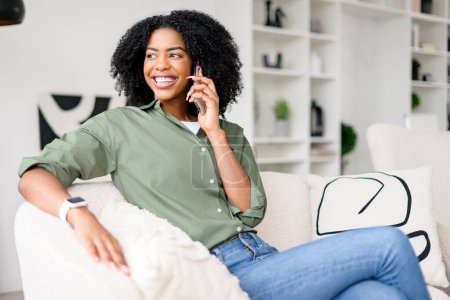 Photo for Caught mid-laughter on a phone call, the woman exudes delight and comfort, with her curly hair perfectly framing her face, encapsulating the ease of connecting with loved ones from home - Royalty Free Image