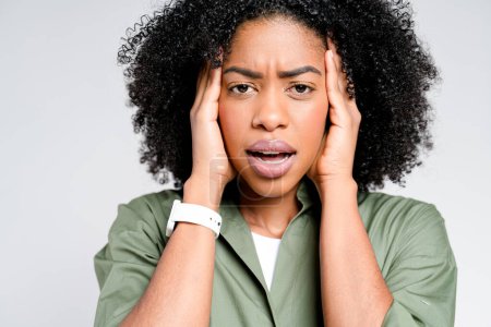 Photo for An African-American woman expresses stress or concern, hands pressed to her temples, her facial expression portraying a moment of anxiety or intense thought against a stark background - Royalty Free Image
