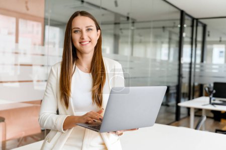 Confident young businesswoman exudes casual professionalism, holds a laptop, ready to present or collaborate. Concept of a streamlined workflow and the mobility of modern work life