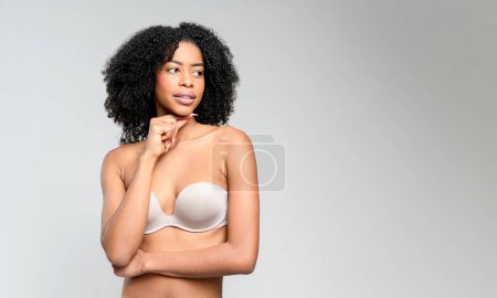 A poised African-American woman with captivating natural curls gazes thoughtfully into the distance. Her hand delicately supports her chin, suggesting a moment of deep reflection