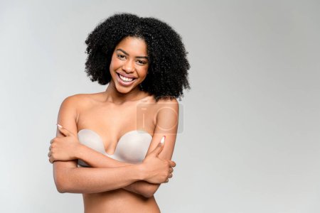 A radiant African-American woman stands with her arms crossed over her chest, sporting a backless adhesive bra, conveying a message of confidence and comfort in ones skin.