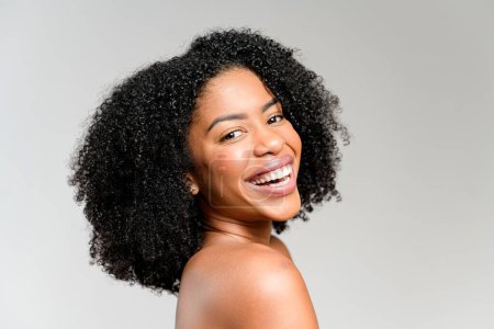 Eine Profilansicht einer afroamerikanischen Frau mit strahlendem Lächeln und üppigem lockigem Haar, die vor einem gedämpften Hintergrund Glück und Positivität ausstrahlt und einen Moment purer Freude einfängt..