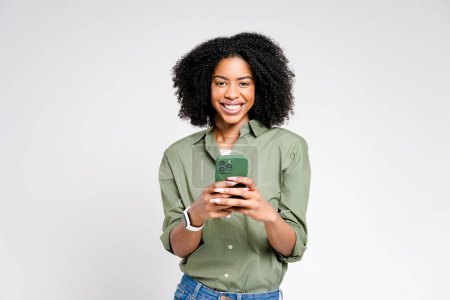 A young African-American woman in a green shirt beams as she holds her smartphone, embodying the connection between technology and daily joy