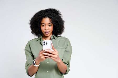 Téléchargez les photos : Une femme afro-américaine contemplative tient étroitement son smartphone, son expression réfléchie, indiquant un moment de décision ou de réflexion. - en image libre de droit
