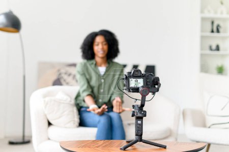 Photo for With a wave and a smile, an African-American woman engages her online audience, creating an inviting atmosphere in her vlog from a minimalist living space - Royalty Free Image