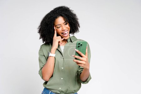 Une pose réfléchie et un doux sourire encadrent cette jeune femme avec son smartphone, suggérant un moment de découverte en ligne agréable