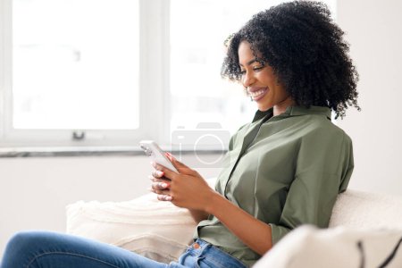 En un momento de serenidad, la mujer está absorta en su smartphone, navegando por la web o leyendo un artículo interesante. La integración del ocio digital en ambientes hogareños tranquilos