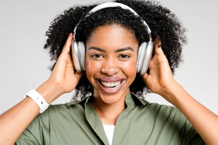 Foto de Una mujer afroamericana alegre disfruta de la música favorita en auriculares plateados, su sonrisa exudando la alegría de la melodía. El estudio captura la esencia del ocio moderno y el entretenimiento digital - Imagen libre de derechos