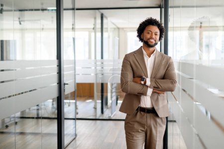 An African-American businessman, start-up owner stands confidently with his arms crossed in a modern office, showcasing a blend of style and professionalism
