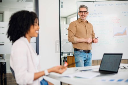 A seasoned leader shares insights with a focused team in a modern office, highlighting a mentorship moment in a professional environment. The diverse team is engaged in an active learning session