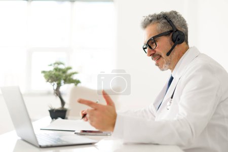 Senior doctor with grey hair is enthusiastically explaining concept during a telehealth session, using his hands to gesture, which reflects a patient-friendly approach to remote medical consultations