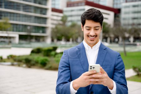 An entrepreneur is captured absorbed in his smartphone, a smile playing on his lips as he stands in a city square, epitomizing the union of business and technology.