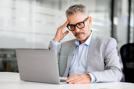 Mature businessman is deeply focused on his laptop screen in a serene office setting, embodying the concentration and strategic thought that drives business success, a moment of deep analysis