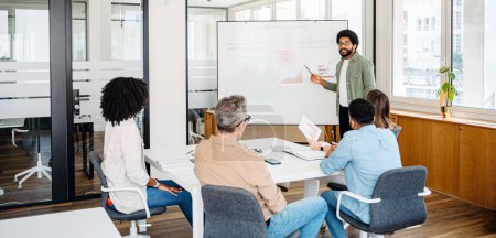 A diverse and dynamic team gathers in a modern office space, where a young professional takes the lead in presenting strategic insights on a whiteboard. The ideas and strategies exchanging