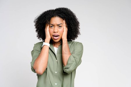 Photo for With an expression of concern, this African-American woman holds her head in her hands, her furrowed brow and pensive look conveying a sense of worry or deep thought on a neutral background - Royalty Free Image