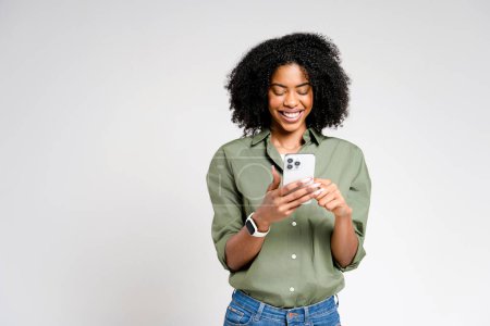 Téléchargez les photos : Une femme afro-américaine rayonnante profite d'un moment lumineux avec son smartphone, son sourire radieux suggérant de délicieuses nouvelles ou un message humoristique - en image libre de droit
