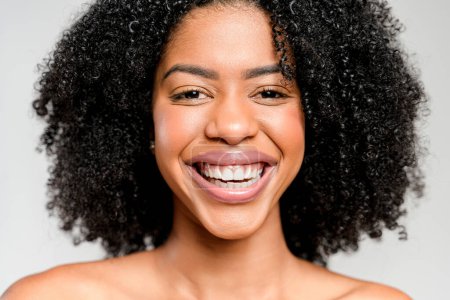 Un primer plano de una cara de mujer afroamericana, su sonrisa amplia y genuina, muestra la belleza radiante y la energía positiva que viene de dentro, complementada por su cabello rizado natural.