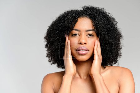 Contemplative African-American woman holds her face in her hands, her gaze introspective and full of depth, against a minimalist backdrop. The image captures a moment of self-reflection and the beauty