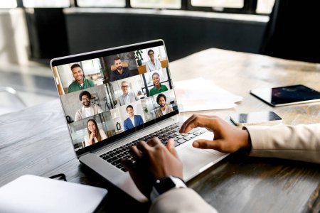 Joven emprendedor se muestra en medio de una alegre reunión virtual, con una pantalla portátil que muestra una galería de caras amigables y diversas. Reunión virtual y concepto de videollamada