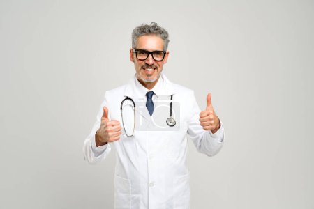 The senior doctor enthusiastic shows thumbs-up suggests a positive outcome or good news, complemented by his friendly expression and professional attire, against a grey backdrop.