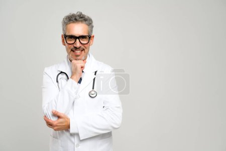 Ein älterer grauhaariger Arzt steht selbstbewusst mit einem Stethoskop um den Hals, lächelt freundlich in die Kamera und strahlt Vertrauen und Professionalität aus..