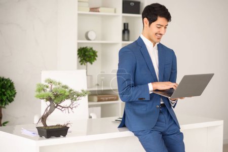 Young Hispanic businessman works attentively on his laptop, fully engaged in his task amidst a tastefully decorated office, represents dedication and seamless integration of technology in business
