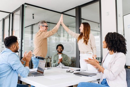 In a spirited office atmosphere, colleagues share a high-five, celebrating a successful moment with clapping and smiles, highlighting the camaraderie and success within the team